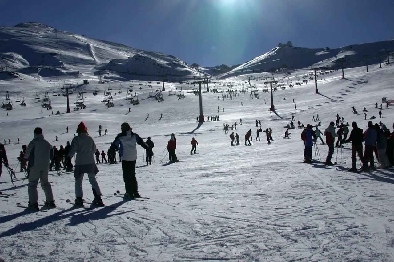 "Many people learning how to ski in Sierra Nevada (Granada, Spain). Backlight from Monachiles. On the left you can see the Veleta peak. It is one of the highest altitudes of the PenA-nsula IbArica, and being so far south, there are usually many days of sun to the year. From the summit you can see the sea."